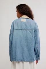 Campera de denim oversize color celeste, con hombro caído, cuello de lona beige en contraste, bolsillos frontales asimétricos, cierre frontal con botones y puños abotonados.
