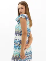 Vestido midi confeccionado en tejido de punto calado, con patrón geométrico en zigzag en tonos blanco, marrón, tostado y azul. Presenta escote a la base, mangas cortas con volados en los hombros, silueta recta y forro interior a tono. Incluye un cinturón fino con hebilla metálica.