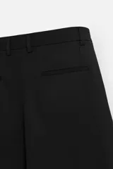 Bermuda de corte relajado color negro, con pliegues frontales, cierre de cremallera y botón, bolsillos laterales y bolsillos traseros.