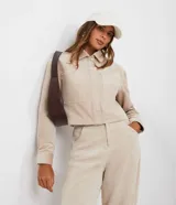 Campera corta color beige de pana con cuello camisero, cierre frontal con botones, bolsillos de parche en el pecho y mangas largas con puños abotonados.