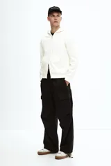 Campera con capucha de algodón pesado, color blanco hueso, de corte holgado y hombros caídos. Posee cierre frontal bidireccional, bolsillos canguro delanteros y puños y bajo acanalados.