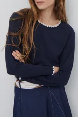 Remera de manga larga en color azul marino, confeccionada en tejido suave. Presenta un delicado detalle de bordado festoneado en color blanco tanto en el cuello redondo como en los puños, aportando un toque distintivo a esta prenda básica.