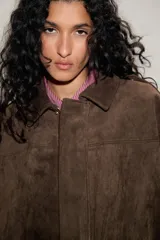Chaqueta de efecto ante color marrón claro, con cuello solapa, manga larga con trabillas en los hombros y bajo abullonado. Cierre frontal con cremallera y botones ocultos por solapa.