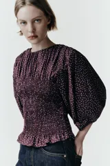 Blusa de color bordó con estampado de lunares claros, confeccionada con cuerpo en nido de abeja elástico, cuello redondo y mangas abullonadas por debajo del codo.
