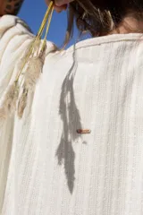 Ruana de tejido liviano con textura acanalada, de caída suave y diseño holgado. Presenta una pequeña placa metálica con el logo de la marca en la parte posterior.