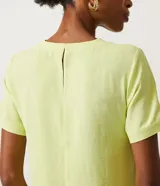 Blusa blanca de poliéster con cuello redondo, mangas cortas, cierre trasero en forma de gota, pequeñas aberturas laterales y acabados en pespuntes en las mangas y el cuello.
