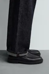 Zapato tipo Mary Jane color negro, con cierre mediante hebilla lateral, parte superior fabricada en piel, detalle de bordón en el empeine, horma redonda y suela con volumen.