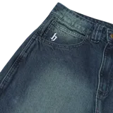 Pantalón de jean azul con efecto lavado y teñido verdoso, de corte amplio y tiro medio.