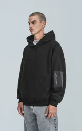 Hoodie oversize de algodón, color negro, con capucha forrada, bolsillo frontal tipo canguro y bolsillo con cierre en la manga estilo bomber.