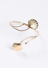 Brazalete abierto para brazo en tono dorado, con diseño entrelazado y dos dijes en forma de concha marina en los extremos.