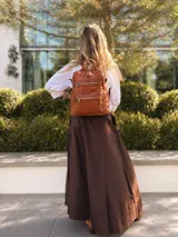 Mochila de símil cuero color suela, con apertura superior, tres bolsillos frontales con cierres metálicos y bolsillos laterales. Incluye correas ajustables para la espalda y una correa larga de galón para usar como bandolera.