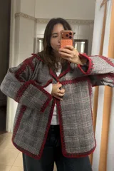 Chaqueta reversible de paño, con un lado gris oscuro con costuras decorativas en hilo rojo y el otro lado con estampado de cuadros. Presenta corte holgado, mangas largas y diseño abierto.
