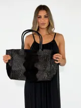 Cartera tipo tote bag de cuero color negro, con textura símil cocodrilo en los laterales y franja central de gamuza. Cuenta con doble asa de hombro.