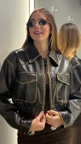 Campera corta de cuero sintético en color negro con efecto desgastado en los bordes y costuras. Presenta cuello clásico, cierre frontal metálico, dos bolsillos delanteros con solapa y cintura elástica.