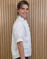 Camisa de denim de algodón celeste, con cierre frontal de botones, cuello alto con volados y mangas cortas abullonadas con puños elastizados fruncidos.