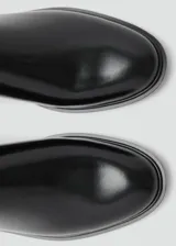 Botín tipo Chelsea de cuero vacuno color negro, con paneles laterales elásticos y tirador trasero. Presenta una silueta clásica con punta redondeada y suela plana de resina de poliuretano.