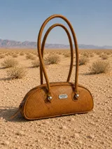 Cartera estilo baguette de cuero, con diseño estructurado y silueta alargada. Presenta manijas largas con detalles de nudos esféricos metálicos en la unión.