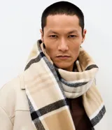 Bufanda de punto suave con estampado de cuadros en tonos beige, blanco y negro, con terminaciones de flecos en los extremos.