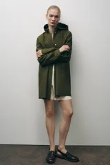 Cazadora impermeable de acabado engomado en color amarillo, con capucha ajustable, cierre frontal con botones a presión, bolsillos laterales y mangas largas ajustables.