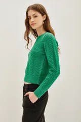 Sweater de punto color verde con diseño de ondas en relieve y sutiles destellos de lentejuelas integradas. Presenta cuello redondo, mangas largas y puños acanalados.