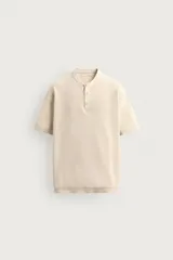 Camiseta regular fit de punto tejido en hilatura de algodón de color beige, con cuello redondo y cierre frontal de botonadura tipo panadero, manga corta y acabados en rib.