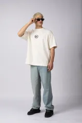 Remera de corte oversize confeccionada en algodón premium de alto gramaje. Presenta un diseño minimalista con un pequeño logo bordado en el centro del pecho y un parche estampado en la espalda. Posee cuello redondo y mangas cortas con caída relajada.