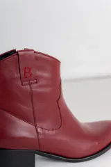 Botas cortas de cuero color marrón, con taco cuadrado y punta fina. Presenta una pieza dorada en la parte superior y un logo en el lateral.