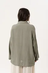 Camisa verde militar de manga larga con silueta oversize, dos bolsillos delanteros y corte levemente más largo en la espalda. Escote en V abotonado con detalle de galón picot a lo largo de la cartera y botones a tono. Isotipo bordado en la parte trasera.