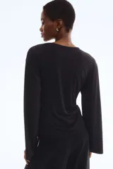 Top negro de manga larga con escote redondo y un nudo ajustable en el lateral inferior.