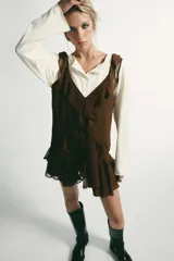 Vestido corto color marrón con escote en pico y tirantes anchos. Presenta un diseño con múltiples volantes en cascada que recorren el frente y el bajo, con un acabado asimétrico.