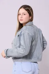 Campera de jean de lavado celeste claro, con diseño clásico de cuello y botones metálicos. Presenta detalles de pequeños brillos o tachas plateadas sobre la tela, especialmente visibles en los bordes de los bolsillos y costuras.