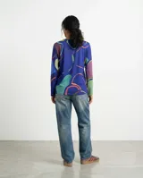 Remera de manga larga con cuello redondo, confeccionada en jersey suave con un diseño estampado de líneas orgánicas en tonos azul, verde y violeta. Presenta un corte recto y cómodo, ideal para uso versátil.