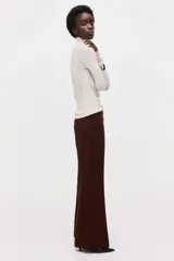 Pantalón acampanado de color bordó, de talle alto con pretina prolongada y cierre oculto. Presenta bolsillos al bies en los laterales, bolsillos decorativos en la parte trasera y perneras amplias con pliegues marcados tanto en el frente como en la espalda.