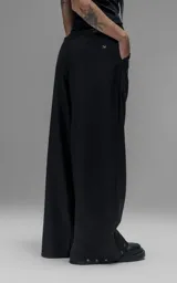 Pantalón sastrero de corte oversize, color negro, con pinzas frontales que forman tablones profundos, cintura ancha, presillas robustas y bolsillos laterales y traseros tipo ojal.