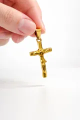 Dije de acero inoxidable con baño dorado en forma de cruz con figura de Cristo en relieve.