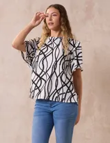 Blusa blanca estampada con líneas y lunares negros, de crepe marca Alex & Parker. Tiene cuello a la base, escote en V con botón y mangas cortas amplias.