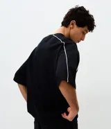 Remera masculina de corte boxy, color negro, con cuello redondo y mangas cortas amplias. Presenta detalles de vivos blancos en contraste a lo largo de las costuras de las mangas y hombros.