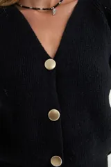 Cardigan negro de tejido de punto, con escote en V, manga larga y cierre frontal con tres botones dorados grandes.