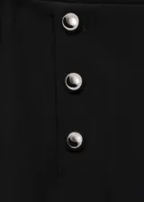 Pantalon de vestir negro de corte wide leg y tiro medio. Presenta un diseño largo con detalle de botones metálicos plateados en la parte frontal y cierre de cremallera lateral.