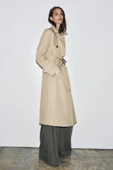 Trench color beige con cuello solapa y manga larga ajustable con trabillas. Bolsillos en delantero. Cinturón en mismo tejido. Detalle de pespuntes marcados a tono. Cierre frontal cruzado con botones. Tejido repelente al agua.