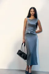 Vestido maxi entallado sin mangas, confeccionado en punto. Modelo con escote asimétrico y detalle de metal en un hombro. Panel drapeado con detalle metálico bajo la cintura para estilizar la silueta.