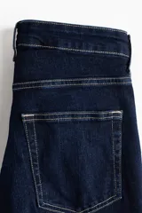 Jean de tiro alto con corte acampanado desde la rodilla, confeccionado en denim azul oscuro con costuras en contraste y diseño de cinco bolsillos.