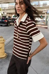 Top de estilo polo con mangas cortas, confeccionado en tejido de punto con diseño de rayas horizontales en tonos marrón y crema. Presenta cuello clásico y puños en contraste de color blanco en popelín, con cierre frontal de un botón y aberturas laterales en el bajo.