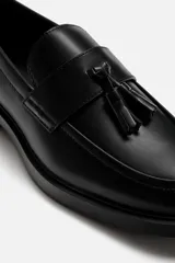 Mocasín de vestir negro con detalle de borlas en la parte superior, forro y plantilla interior a tono, horma redonda y suela con ligero tacón.