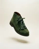 Botas cortas de gamuza color verde militar, con cierre de cordones de cuero y borlas colgantes en el empeine. Presentan punta redondeada y suela plana oscura.