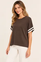 Remera marrón de punto, de corte holgado y manga corta con detalles de rayas blancas en los puños, con cuello redondo.
