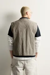 Chaleco de algodón acolchado de corte relaxed fit, color verde militar con efecto lavado. Presenta cuello en V, cierre frontal con cremallera y bolsillos frontales de parche.