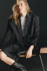 Blazer oversize de corte recto con cuello de solapa, manga larga con hombreras y cierre frontal de doble botonadura. Presenta un diseño en color gris oscuro con costuras decorativas a contraste en color blanco, bolsillos con solapa y forro interior.