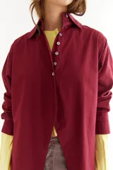 Camisa de algodón color bordó, con cuello clásico, cierre frontal de botones y diseño con recorte diagonal en el frente y aberturas laterales. Presenta un bordado en zigzag en la espalda.