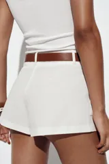 Bermuda blanca de tiro alto con pliegues frontales y bajo ancho. Incluye un cinturón trenzado de cuero marrón con hebilla redonda metálica.